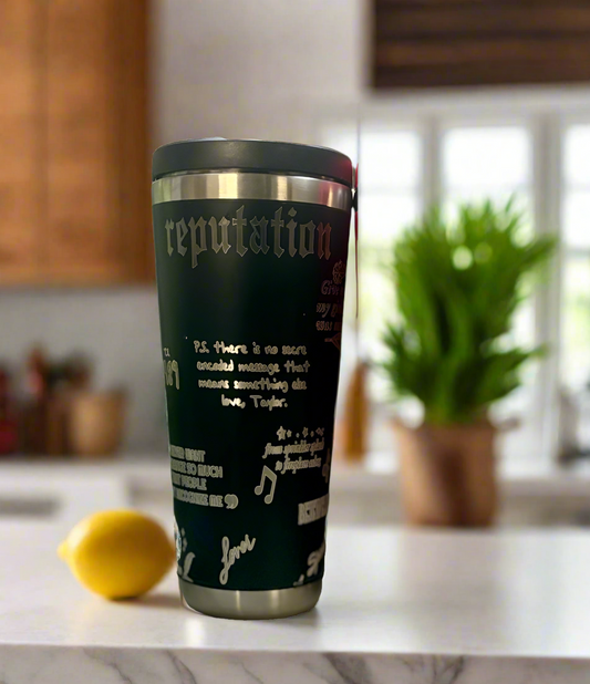 The Kreative Kreationz Taylor Swift Eras 20oz Engraved Tumbler sits on a kitchen counter, personalized with "Reputation"-inspired text and designs. A lemon and a blurred green plant in the background accent the stylish tumbler.