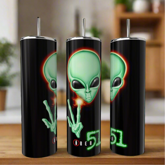 Three black Area 51 20oz Skinny Tumblers by Kreative Kreationz feature a large green alien face making a peace sign, glowing “Area 51” text, and come with reusable metal straws. The eco-friendly tumblers are shown indoors on a wooden surface.
