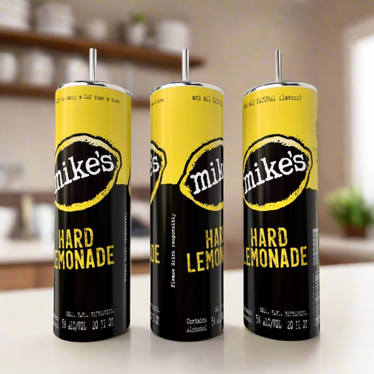 Three Mikes Hard Lemonade cans with yellow and black labels are displayed beside a Kreative Kreationz Mikes Hard Lemonade Variety 20oz eco-friendly stainless steel tumbler, set against a blurred kitchen backdrop with shelves and dishes.