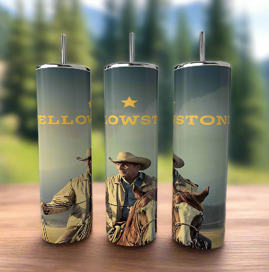 Three Kreative Kreationz Yellowstone 20oz Tumblers sit on a wooden surface, featuring cowboy and horse graphics with bold yellow text. The stainless steel tumblers are set against a blurred forest and mountain backdrop.