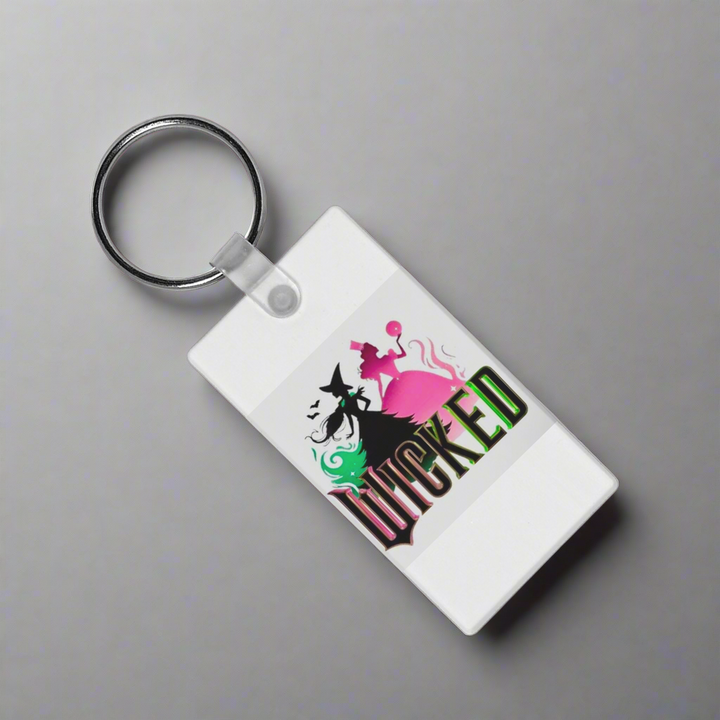 The Kreative Kreationz Wicked Keychain is a sturdy white accessory with vibrant sublimation art of two witches—one green, one pink—and "Wicked" boldly printed below.