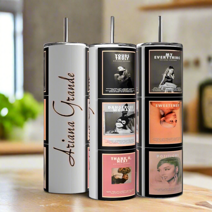 Three Ariana Grande Signature Tumblers by Kreative Kreationz, showcasing her name and album covers, sit on a kitchen counter. These reusable tumblers are eco-friendly and ideal for fans seeking a stylish way to sip their favorite drinks.