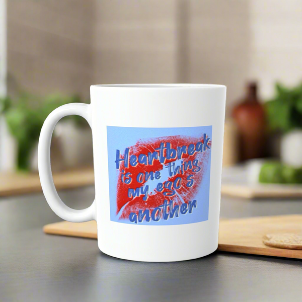The Sabrina Carpenter Ceramic Lips Mug by Kreative Kreationz sits on a kitchen counter, showing red lipstick marks and the quote, "Heartbreak is one thing, my ego's another." This dishwasher-safe mug has green plants blurred in the background.