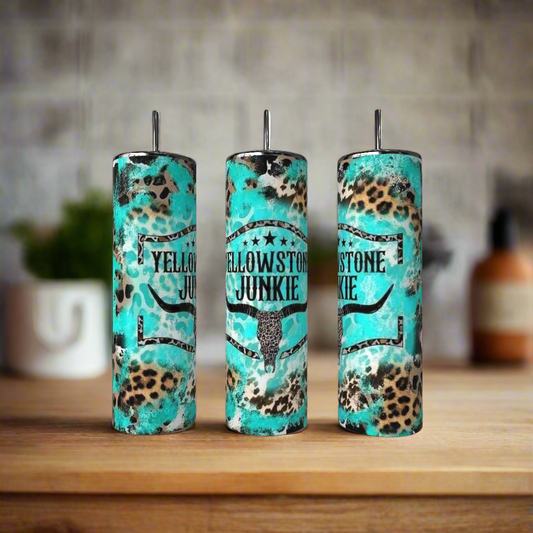 The Kreative Kreationz Teal  20oz Tumbler features a bull skull graphic shown on a wooden surface alongside brown and leopard-print stainless steel tumblers; the background is softly blurred.