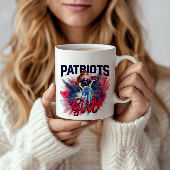 A woman in a white sweater holds the Patriots Girl Ceramic Mug | 11oz by Kreative Kreationz, featuring a sublimated design of a woman in jeans and a Patriots shirt on a red, white, and blue splatter background.