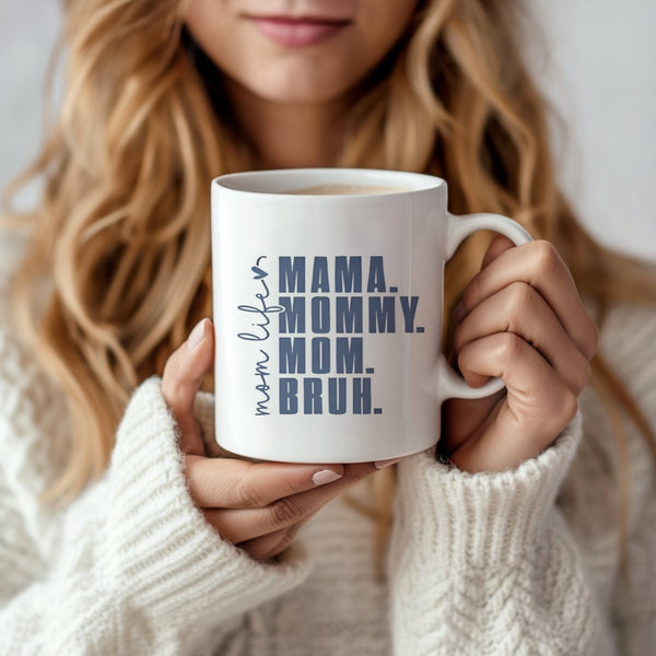 A woman with long blonde hair in a cozy white sweater holds the Kreative Kreationz Mom Bruh Mug, a dishwasher safe ceramic mug featuring "mom life: MAMA. MOMMY. MOM. BRUH." in bold letters.
