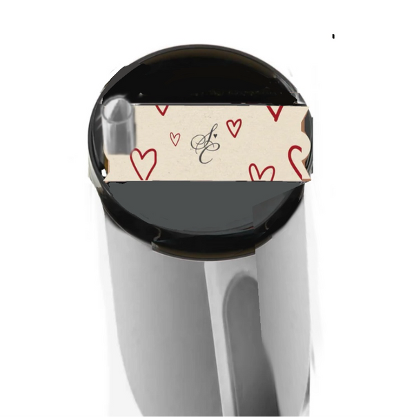 Viewed from above, the Sabrina Carpenter Heart Stanley Lid Topper by Kreative Kreationz features a silver finish with a paper band displaying red hearts and an elegant black "E" on white. This exquisite accessory adds charm to your morning ritual.