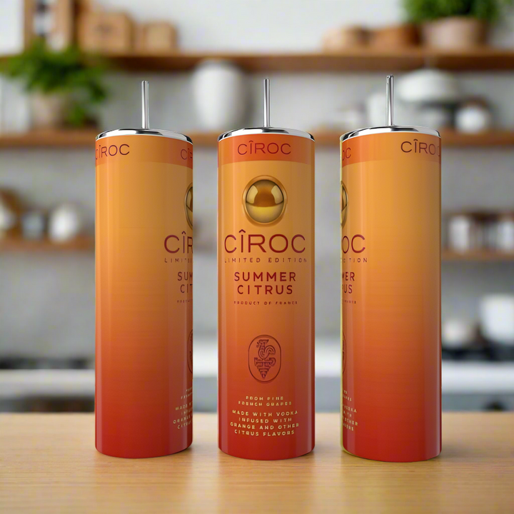 Three tall, slender Kreative Kreationz Summer Citrus 20oz Tumblers with eco-friendly stainless steel straws are displayed on a wooden surface. The orange and gold gradient tumblers stand out against a blurred kitchen background.