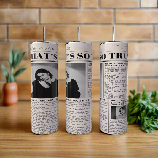 Three Gracie Abrams 20oz Skinny Tumblers by Kreative Kreationz, with pump tops and a vintage column design, rest on a wooden surface; green herbs are to the right, and a tiled wall is in the background.