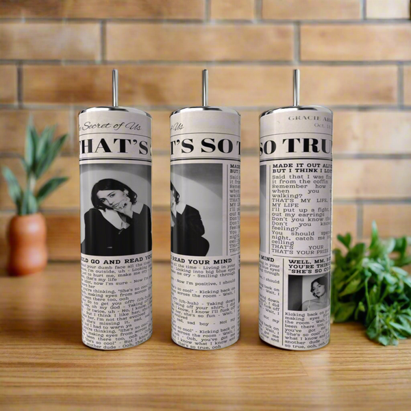 Three Gracie Abrams 20oz Skinny Tumblers by Kreative Kreationz, with pump tops and a vintage column design, rest on a wooden surface; green herbs are to the right, and a tiled wall is in the background.