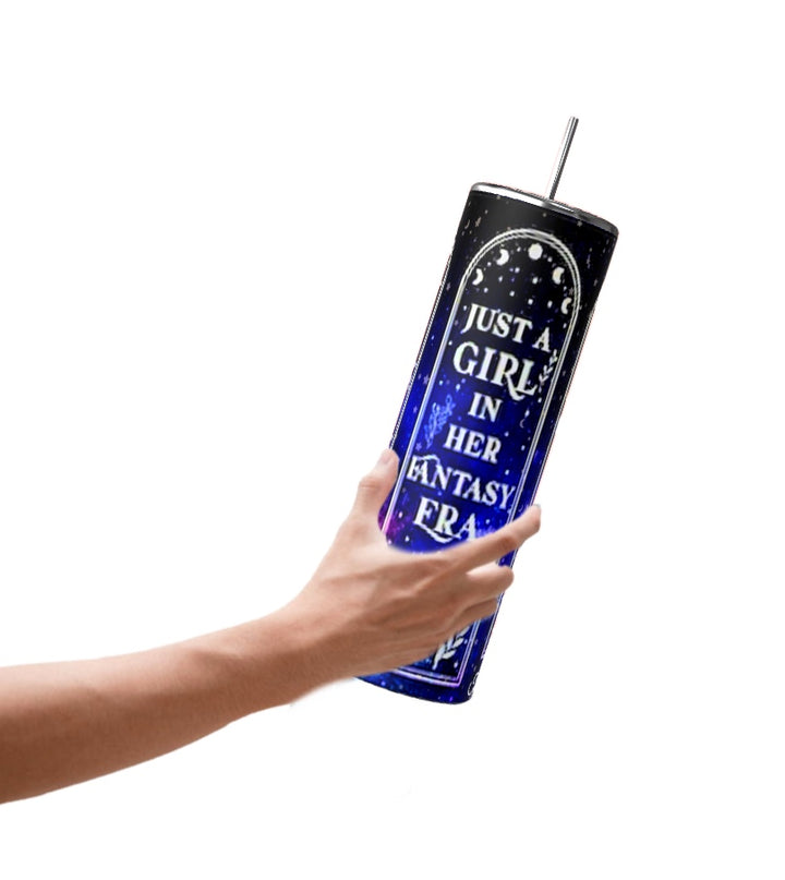A hand holds the stylish Just a Girl 20oz Tumbler by Kreative Kreationz, featuring a dark blue design with a spill-proof lid and straw. The tumbler is decorated with stars and the phrase "Just a girl in her fantasy era" in sharp white letters.