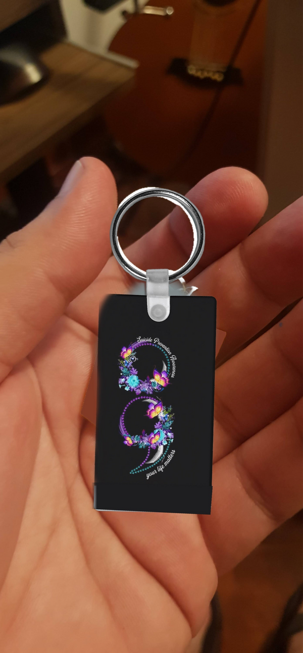 A person holds the Suicide Prevention Awareness Keychain by Kreative Kreationz—a black sublimation accessory featuring a colorful, floral dragon "S" design and curved text, honoring suicide prevention.