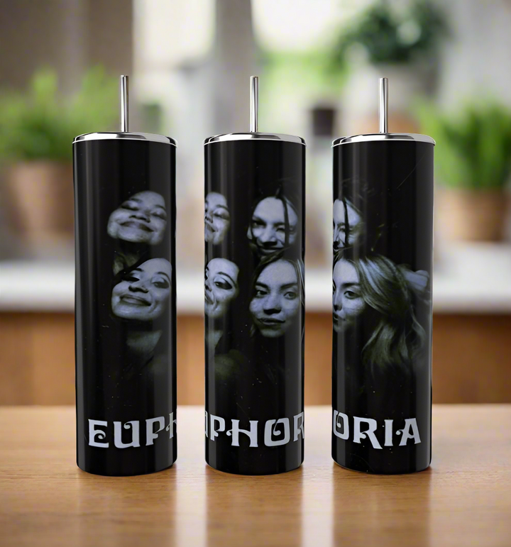 Three eco-friendly 20oz Euphoria tumblers from Kreative Kreationz, crafted from stainless steel, feature black-and-white photos of smiling faces. Each tumbler forms the word "EUPHORIA" and sits gracefully on a wooden surface with blurred green plants behind them.