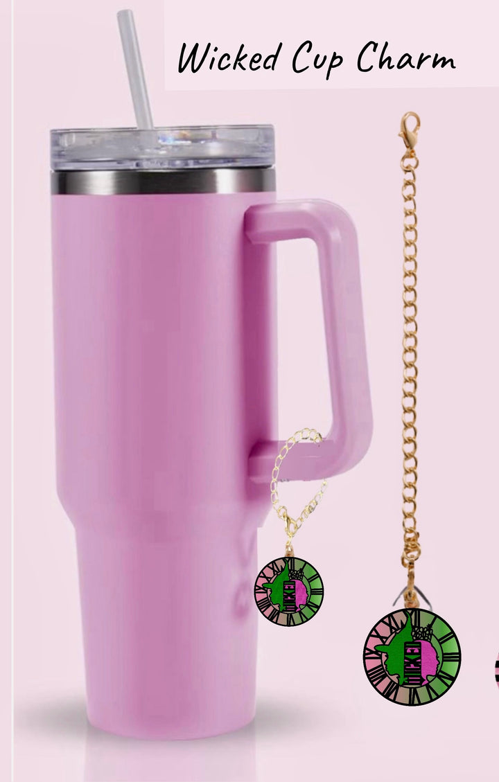 A pink tumbler with a clear lid and straw is shown next to the Kreative Kreationz Wicked l Charm Dangle, featuring a green and purple design with a witch hat motif on a gold lobster clasp chain.