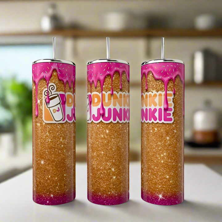 Three Kreative Kreationz Dunkin Junkie 20oz Tumblers with glitter, pink dripping tops, bold “Dunkin Junkie” text, and a coffee cup icon are displayed on a kitchen counter with a blurred background.
