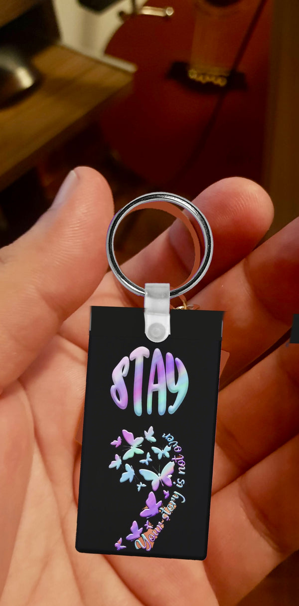 A hand holds the Semicolon Suicide Prevention Awareness Keychain by Kreative Kreationz, featuring colorful pastel letters spelling "STAY," birds, hearts, a semicolon symbol, and "be happy" in cursive to support suicide prevention awareness.