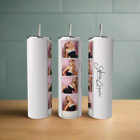 Three white Sabrina Carpenter Photo Strip Tumblers by Kreative Kreationz, each with a silver straw, eco-friendly design, and photo strip of Sabrina Carpenter posing against pink, plus her signature, are displayed on a wooden surface.