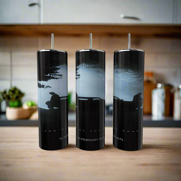 The Kreative Kreationz Supernatural 20oz Skinny Tumbler features a luxury car silhouette with two people on its hood under a cloudy sky, crafted from eco-friendly stainless steel and paired with straws. Background: kitchen countertop, blurred objects.