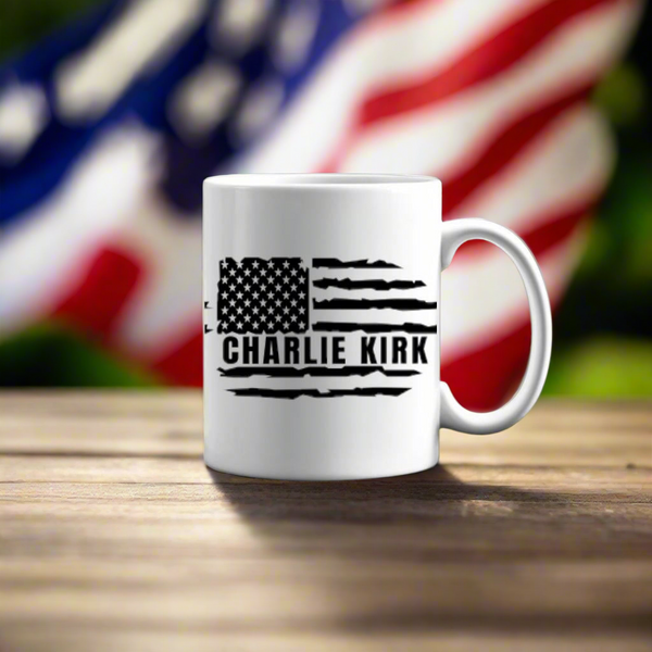 The Charlie Kirk Flag Ceramic Mug by Kreative Kreationz features a black American flag design and his name, displayed on a wooden surface with a blurred flag backdrop—an ideal tribute for expressing your patriotic spirit.