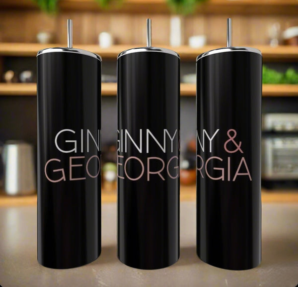 Three Ginny & Georgia 20oz tumblers by Kreative Kreationz, made of black stainless steel and featuring silver straws, sit on a kitchen counter. Each eco-friendly item is labeled in bold letters with shelves blurred in the background.