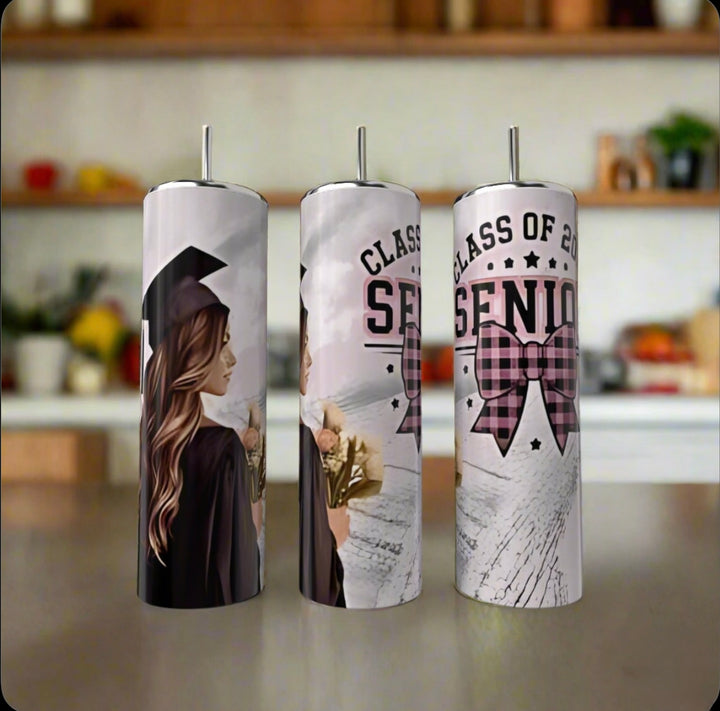 Three Kreative Kreationz 2025 Graduate 20oz Tumblers with lids and straws sit on a counter, featuring a cap-and-gown grad, “Class of 2025 Senior,” a pink plaid bow, and an eco-friendly design. Perfect gift for the graduating senior!.