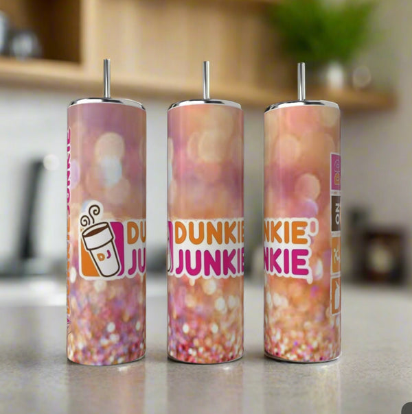 Three Kreative Kreationz Dunkin Junkie 20oz Tumblers with reusable straws sit on a counter. Each features a pink, orange, and white gradient design, “DUNKIN JUNKIE” text, and a coffee cup graphic for a fun touch.