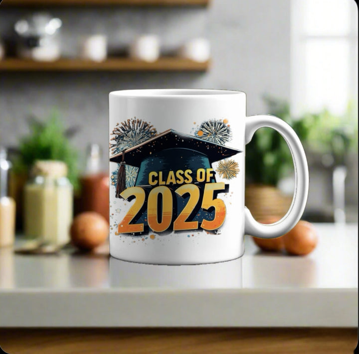 A Kreative Kreationz Class of 2025 Graduate Mug sits on a kitchen counter, featuring a graduation cap and fireworks. Blurry kitchen items are visible in the background. Satisfaction Guaranteed with every purchase.
